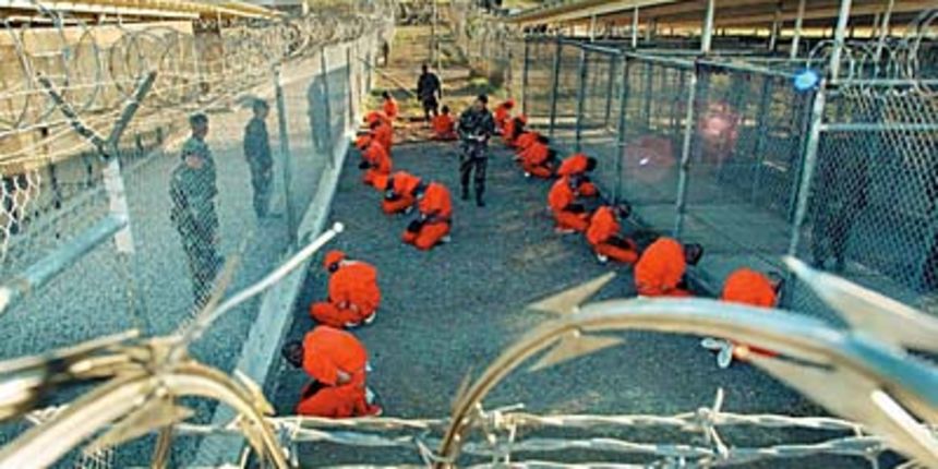 In this photo released 18 January 2002 by the Department of Defense, Al-Qaeda and Taliban detainees in orange jumpsuits sit in a holding area under the surveillence of US military police at Camp X-Ray at Naval Base Guantanamo Bay, Cuba, during in-processi