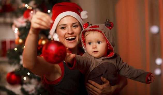 Happy mother showing Christmas ball  to baby near Christmas tree