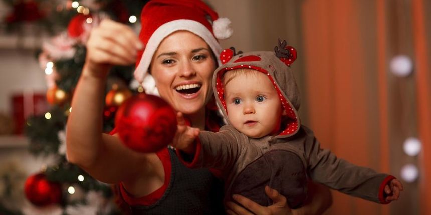 Happy mother showing Christmas ball to baby near Christmas tree Happy mother showing Christmas ball to baby near Christmas tree